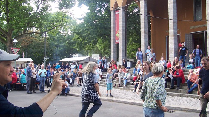 Menschen tanzen auf der Straße vor einem Gebäude mit vielen Zuschauern
