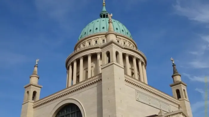 Große Kathedrale mit einer markanten grünen Kuppel und klassischen architektonischen Elementen vor einem klaren blauen Himmel.