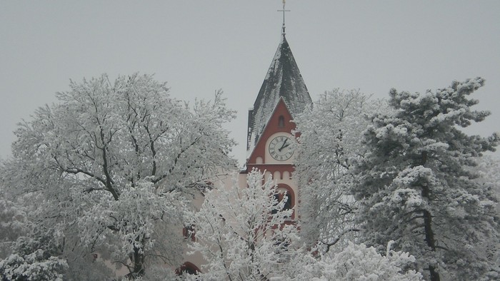 Weißer Schnee bedeckt die Landschaft um die rote Kirchturmuhr.