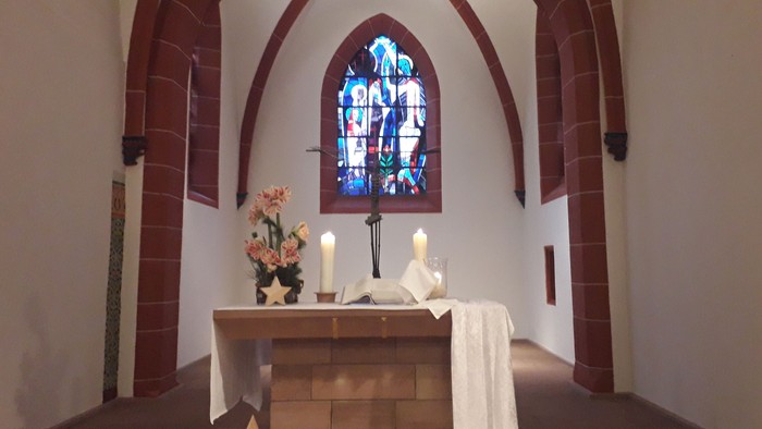 In der Kirche steht ein Altar mit Kerzen und Blumen vor einem buntem Fenster.