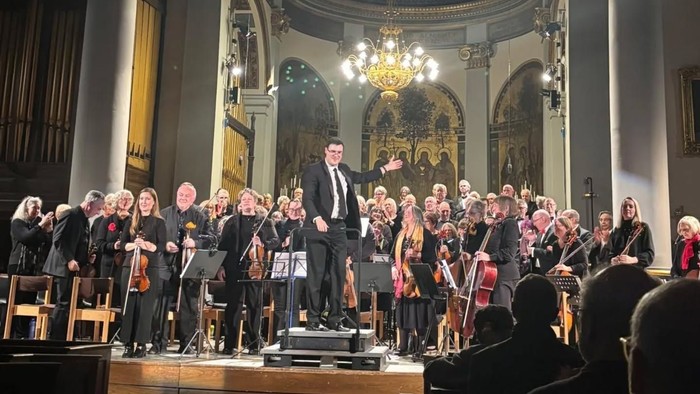 Orchestra performing in an ornate concert hall with classical architectural details and chandeliers.