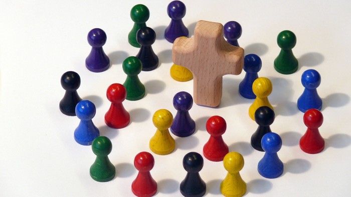 Bunte Spielfiguren stehen um ein Kreuz