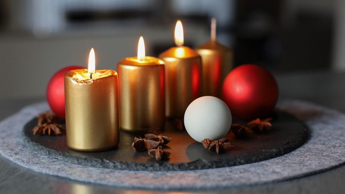 Drei brennende Kerzen in goldener Farbe auf einem Adventsteller