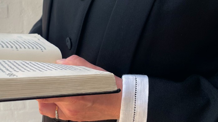 En person i mørk jakke holder en åben bog.