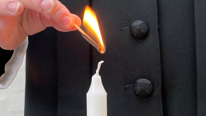 En hånd holder en tændt opfyldning over en lysstake.