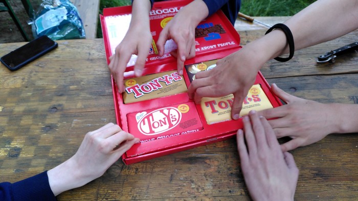 Mehrere Hände greifen in eine rote Schachtel mit Tony's Chocolonely Schokolade