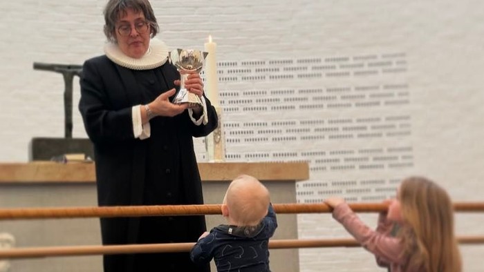 En kvinde i mørkt kapittel holder en trofæ, mens et barn og en pige sitter på en benk.