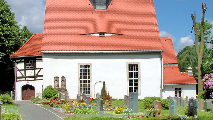 Kleine weiße Kirche mit rotem Dach und schwarzem Turm.
