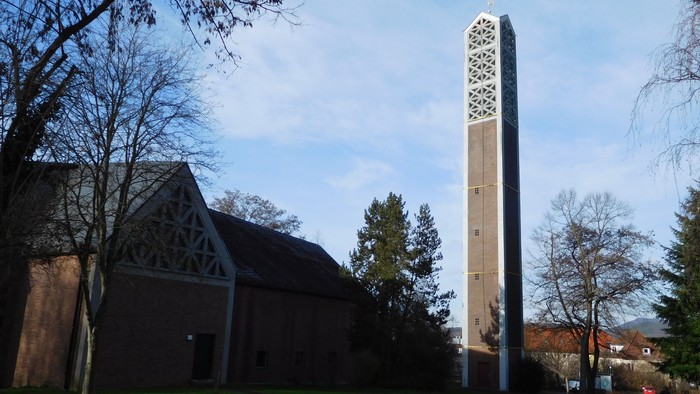 Kirche mit hohem Glockenturm in einer grasbewachsenen Fläche.