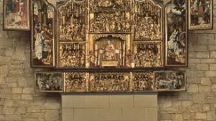 Das Bild zeigt einen verzierten Altar mit mehreren religiösen Darstellungen an einer Kirchenwand.