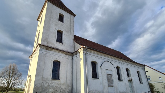 Alte Kirche mit hohem Turm auf grasigem Hügel unter bewölktem Himmel