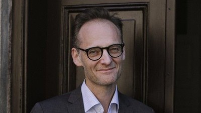 En mand med briller og anzug står foran en dør.