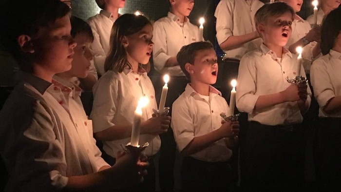 Børn synger med lysende lygter i mørke kirke.