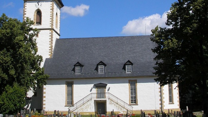 Weiße Kirche mit hohem Turm und Friedhof davor