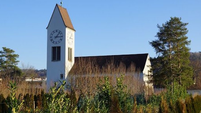 Weißer Kirchturm mit Uhr in ländlicher Umgebung