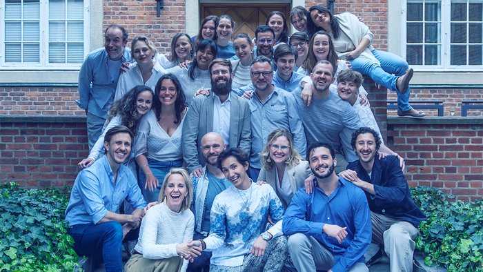 En stor gruppe af venner eller familie poserer til et billede foran et rødt murstenshus.