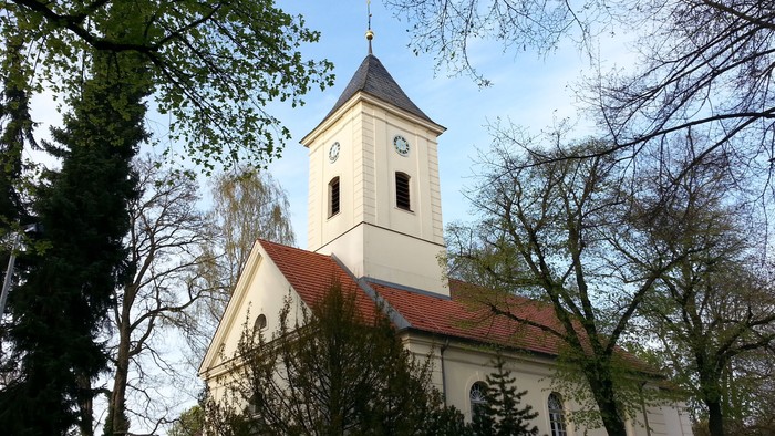 Weiße Kirche mit Uhrturm und rotem Dach zwischen Bäumen