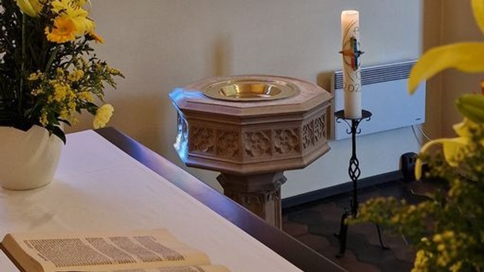 Buntes Kirchenfenster, Taufbecken und Blumenarrangement