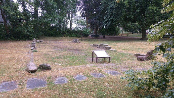 Ein grasbewachsener Friedhof mit alten Grabsteinen und Bänken.