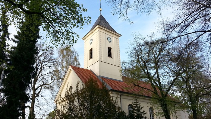 Weiße Kirche mit Uhrturm und rotem Dach zwischen Bäumen