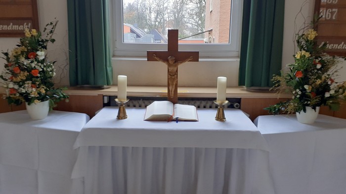 Ein Altar in einer Kirche mit Kreuz, Kerzen und Blumen.