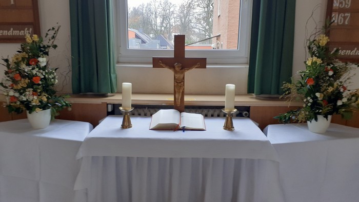 Ein Altar in einer Kirche mit Kreuz, Kerzen und Blumen.