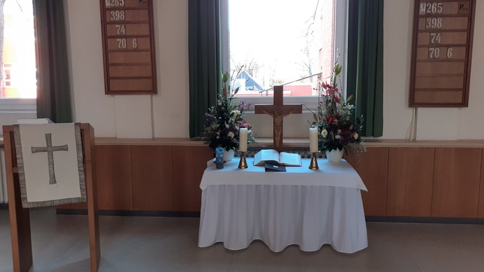 Ein Tisch mit weißer Tischdecke und Blumen in einem Raum mit zwei Kreuzen und Fenstern