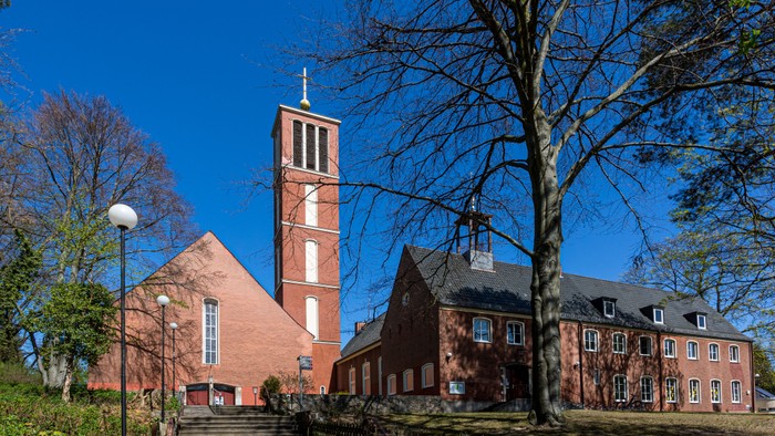 Historische Backsteinkirche mit hohem Glockenturm, umgeben von grünem Laub an einem klaren Tag.