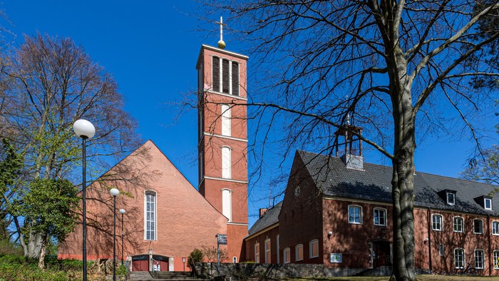 Ein rotes Backsteingebäude mit hohem Turm und Kirche, umgeben von Bäumen unter klarem blauem Himmel