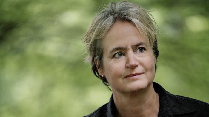 En kvinde med kort, grå hår ser direkte i kameraet.