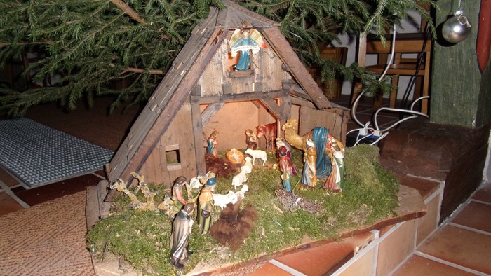Eine Krippe mit verschiedenen Figuren und einem kleinen Stall, umgeben von grünen Pflanzen.