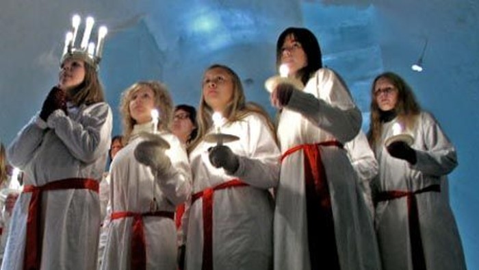 En gruppe kvinder i hvide kler med røde bælter står sammen og ser opad.