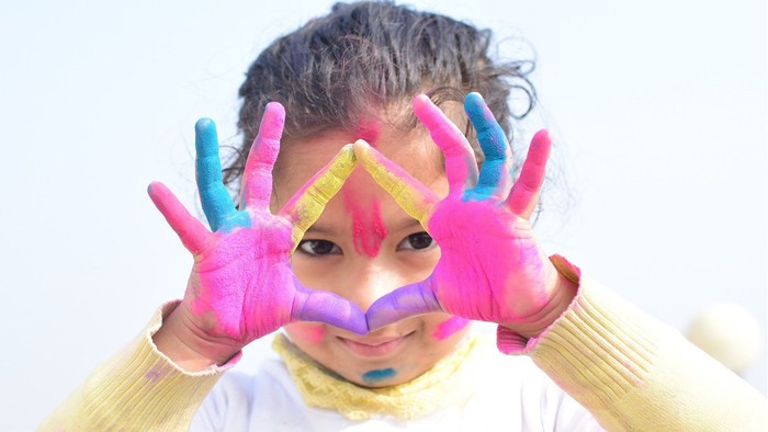 Ein Kind mit bunten Handschuhen und einer bunten Nase macht ein lustiges Gesicht.