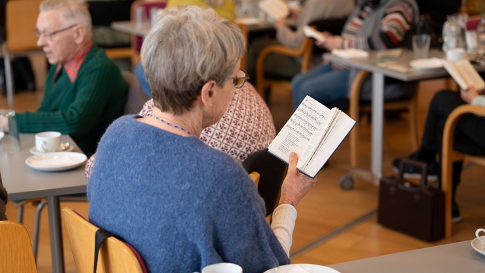 En kvinde læser bog i café, mens andre gæster sidder ved bord.