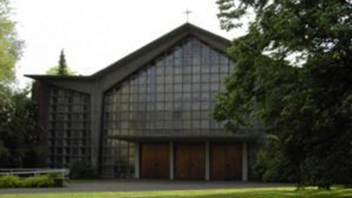 Moderne Kirche mit Glasfassade, eingebettet in eine üppige, grüne Außenanlage.