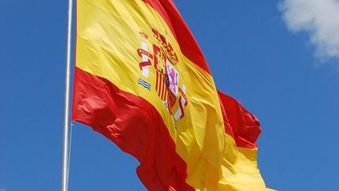 Spanische Flagge, die vor einem klaren blauen Himmel mit vereinzelten Wolken weht.