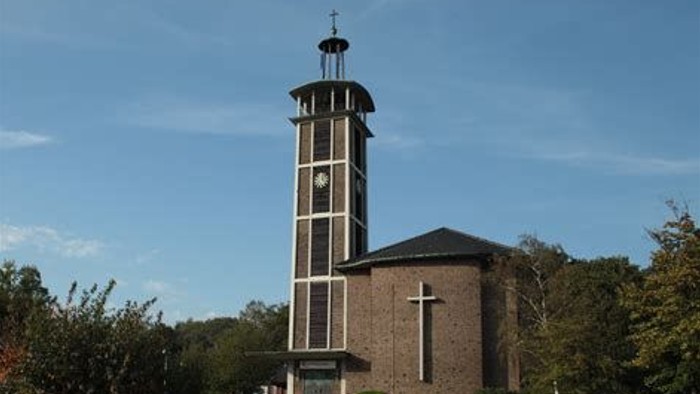 Ein moderner Kirchturm mit Uhr und Kreuz vor grünem Hintergrund