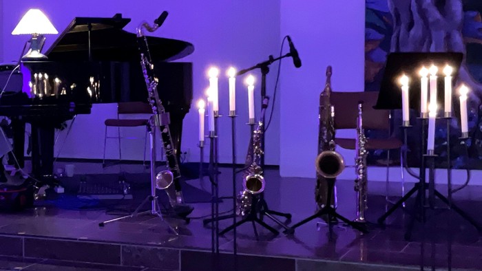 En mørk scene med uddannede blæserinstrumenter og en piano ved lyset af candelabre.