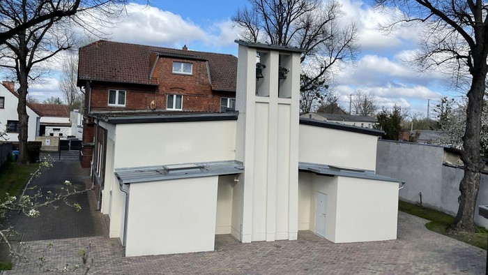 Modernes weißes Gebäude mit einzigartiger Architektur, umgeben von Bäumen und anderen Häusern.