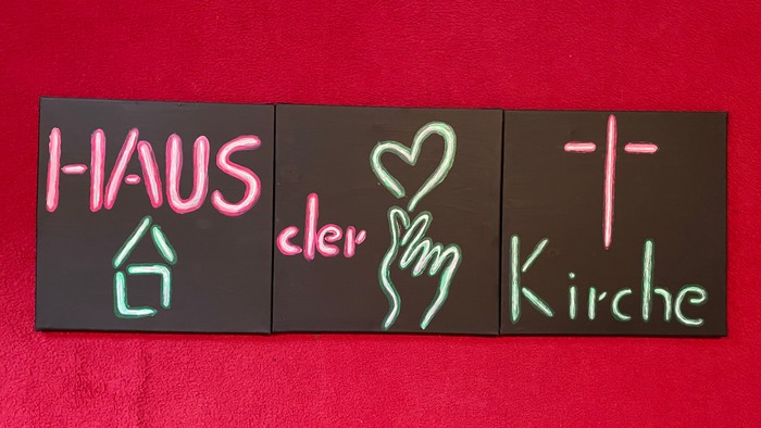 Das Neon-Schild zeigt "HAUS der Liebe Kirche" auf schwarzem Hintergrund