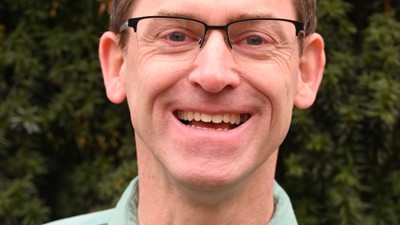 Ein Mann mit Brille und Krawatte lächelt in die Kamera.