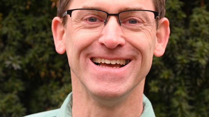 Ein Mann mit Brille und Krawatte lächelt in die Kamera.