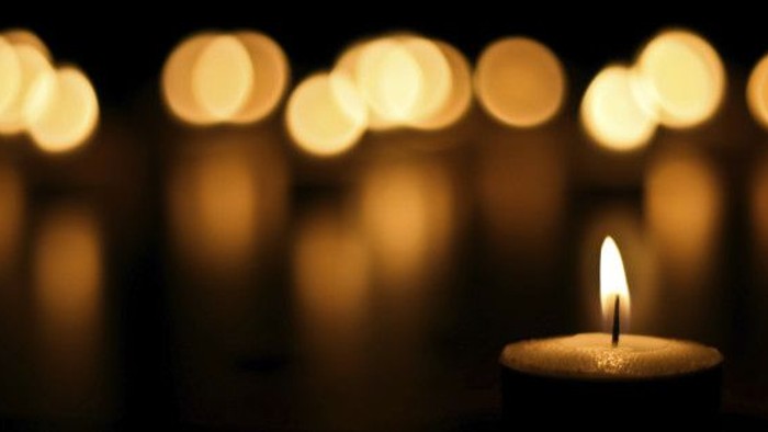 A single lit candle in the foreground with blurred candles in the background.