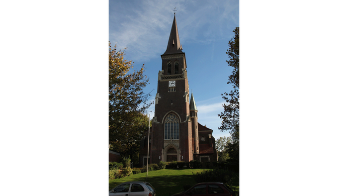 Kirche mit hohem Kirchturm und parkenden Autos in der Nähe.