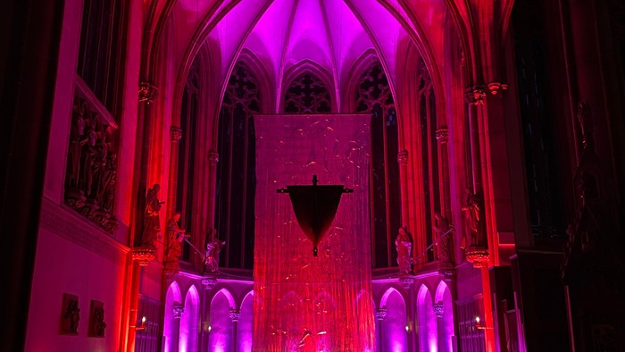 Dramatisch beleuchtetes Inneres einer gotischen Kathedrale mit lebhaften roten und violetten Lichtern.