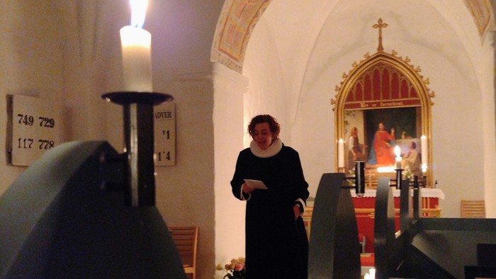 En kvinde i sort kappe står i en kirke ved en lysestøbe.