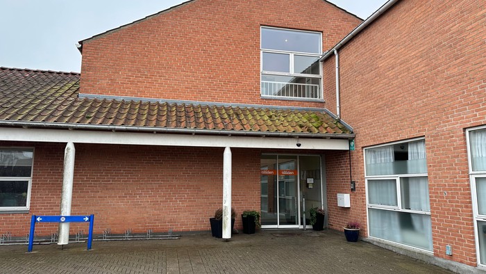 Det er et rødt murstenshus med en indgang og en balustrade.