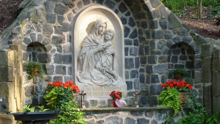 Steinbogen mit Marienstatue und Blumen in Garten