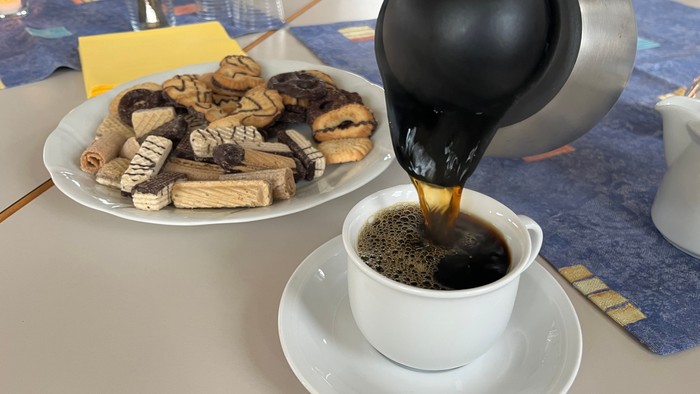 Hier sieht man einen Teller voll mit Keksen und wie eine Tasse Kaffee eingegossen wird.