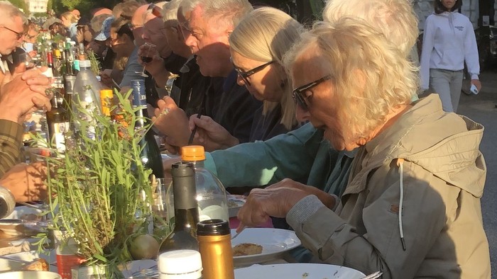 En gruppe mennesker spiser udendørs, der er stilleben og grønne flasker på bordet